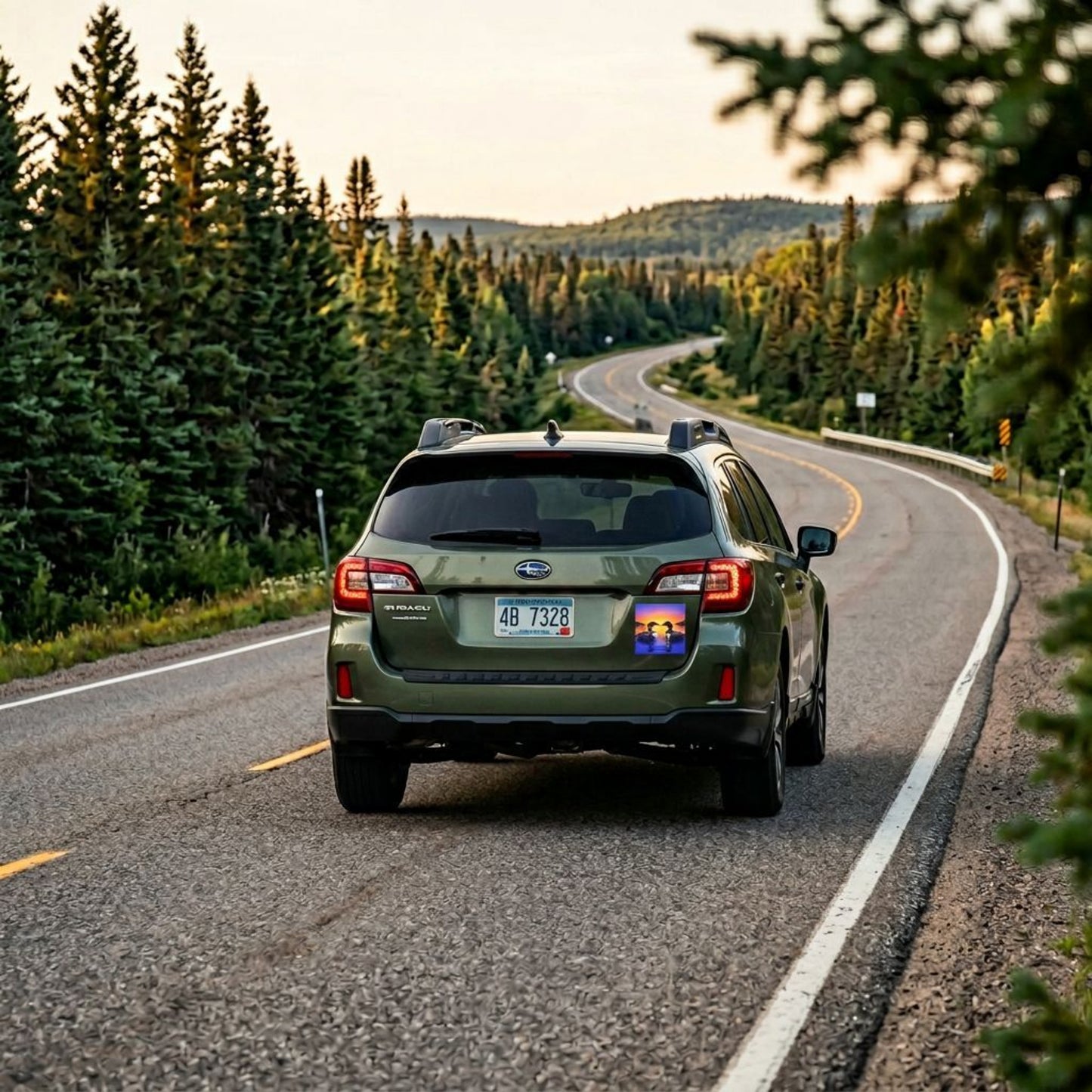 Green SUV driving on a scenic road with trees on both sides. On left side of the back of car, there is a sunrise loon car magnet.