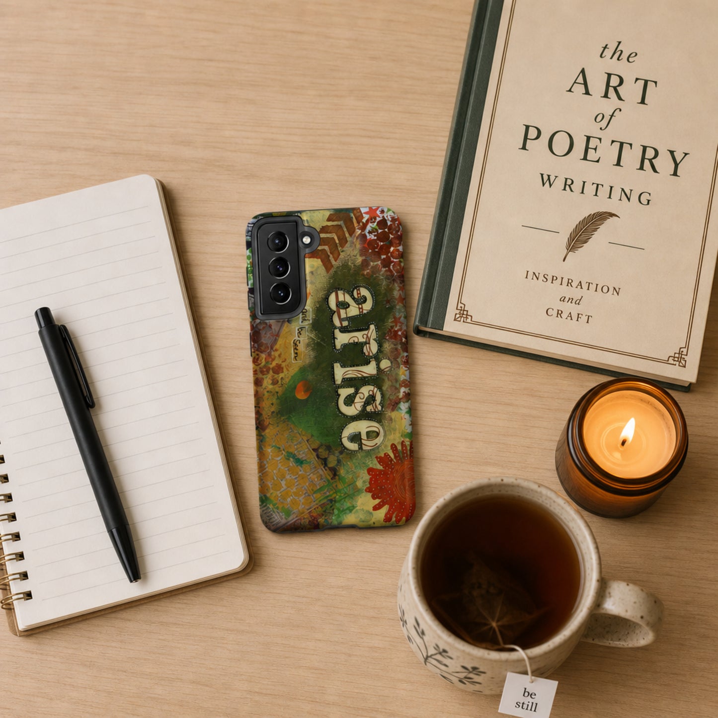 Phone with 'arise' case, notebook, pen, mug with tea, and candle on a wooden surface.