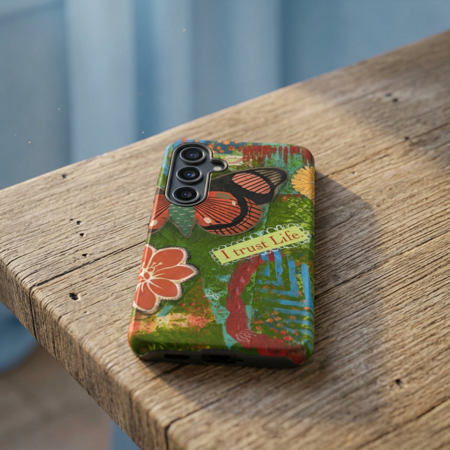 view of artistic butterfly phone case laying on wooden bench. Turquoise, green  and Rusty Orange hues on mixed media art phone.
