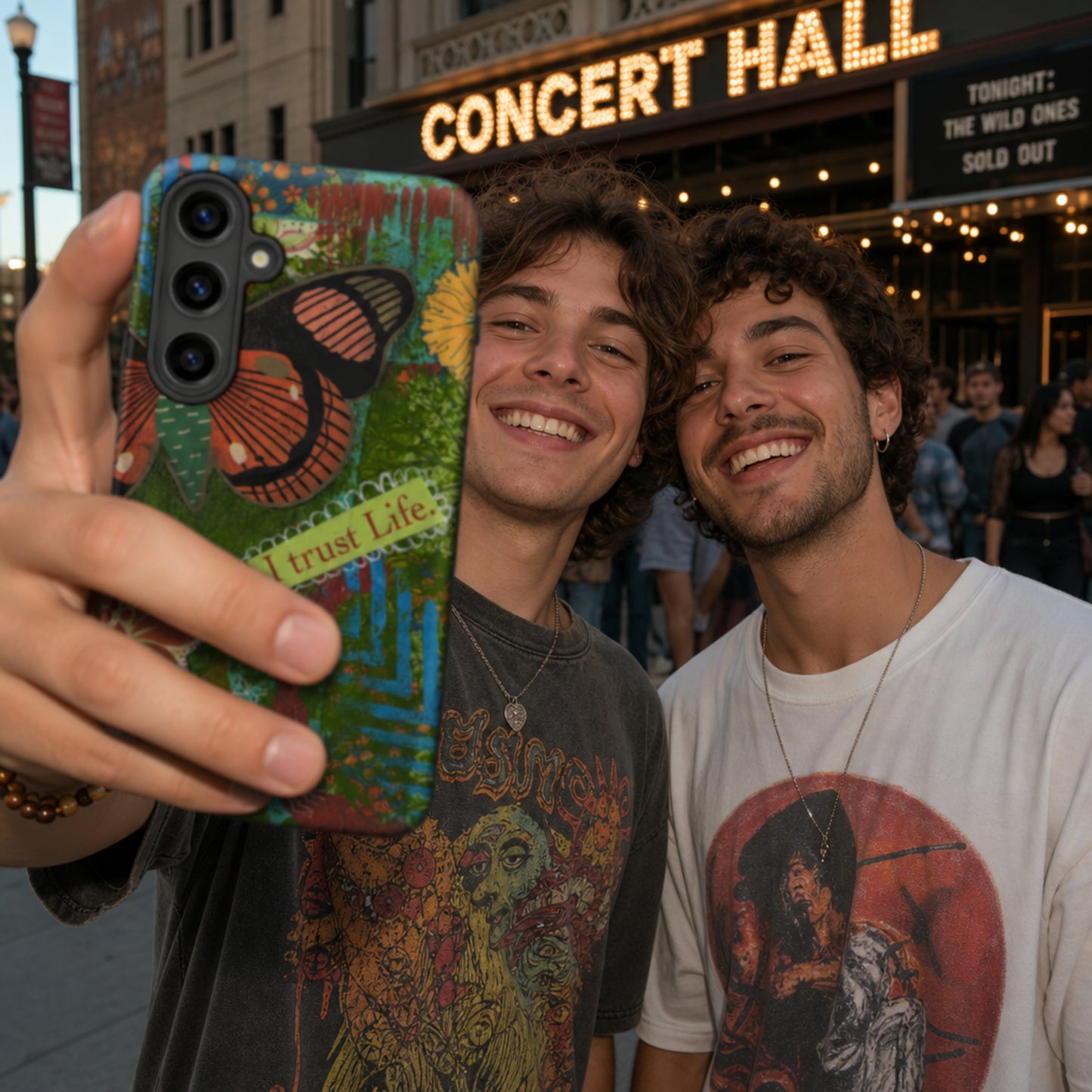 Two men holding up phone for selfie. artistic butterfly phone case has Turquoise, green  and Rusty Orange hues on mixed media art phone.