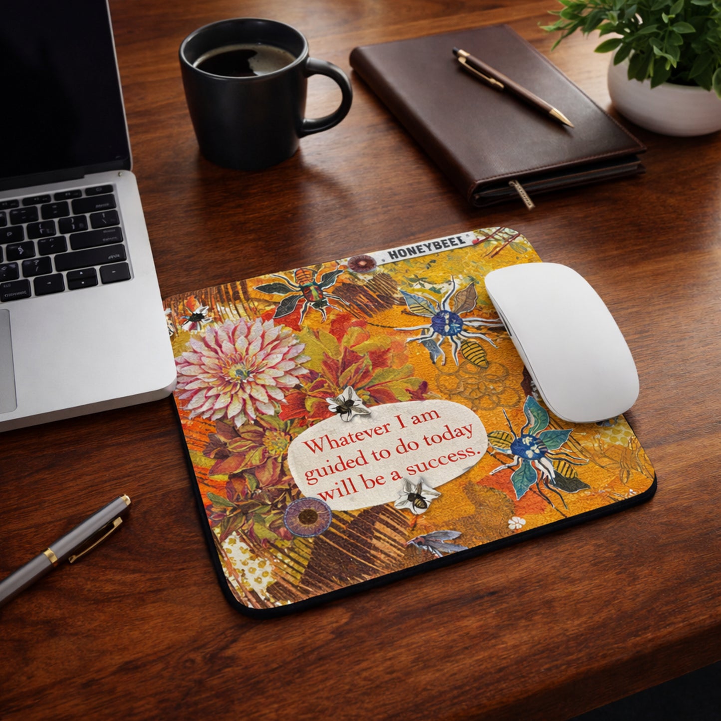 Decorative mouse pad with motivational quote on a wooden desk with laptop, mug, and notebook.