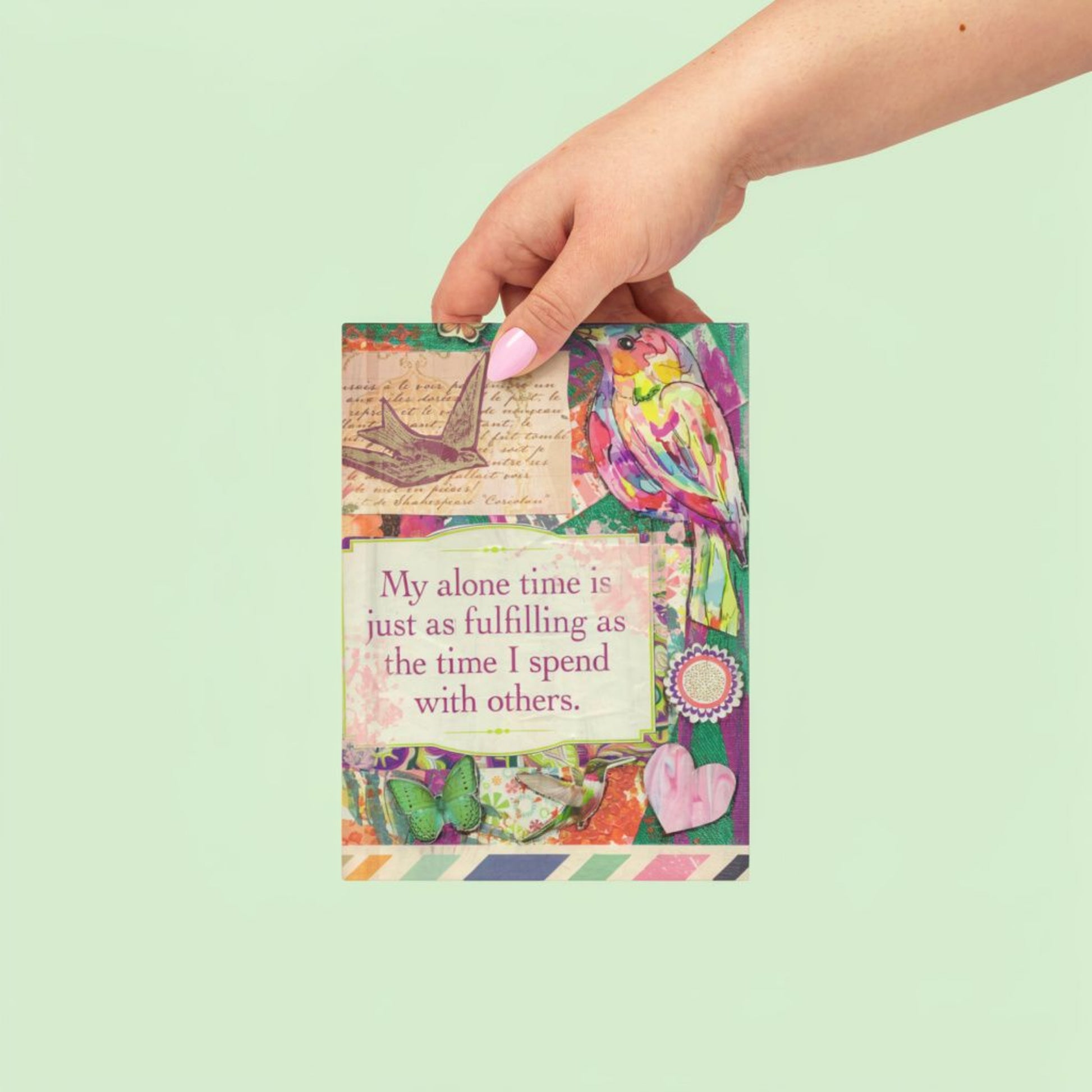 Hand holding the colorful journal with a quote on a light green background