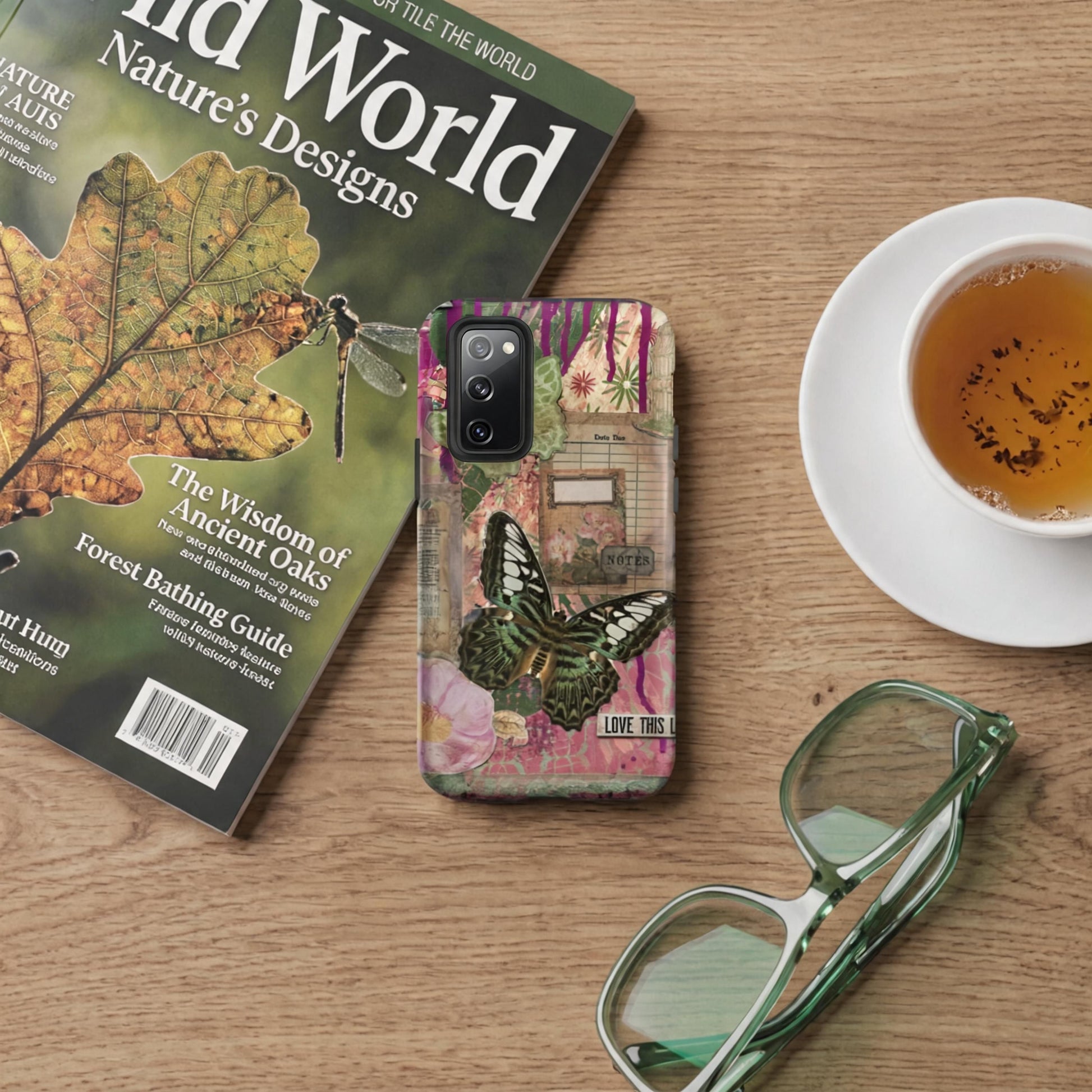 a pink floral butterfly Samsung case love this life quote on a wooden table with a cup of tea, magazine and green eyeglasses.