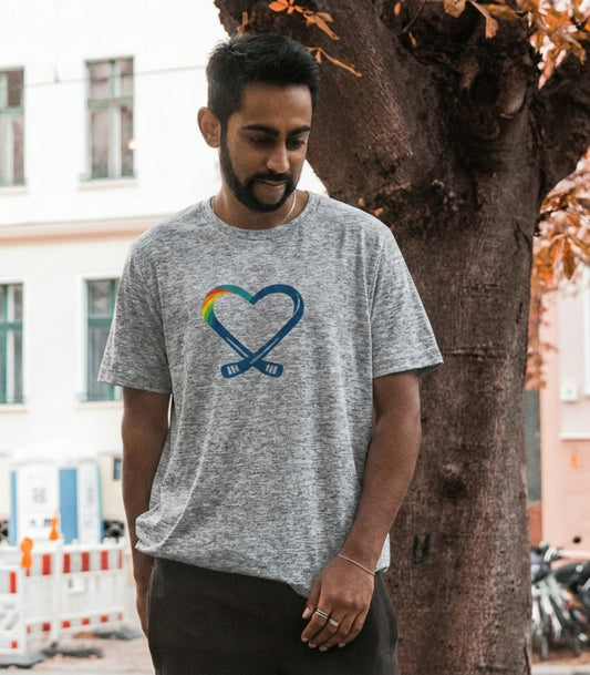 Man wearing a gray colored inclusive hockey logo t-shirt with a hockey stick heart and rainbow design, standing outdoors.