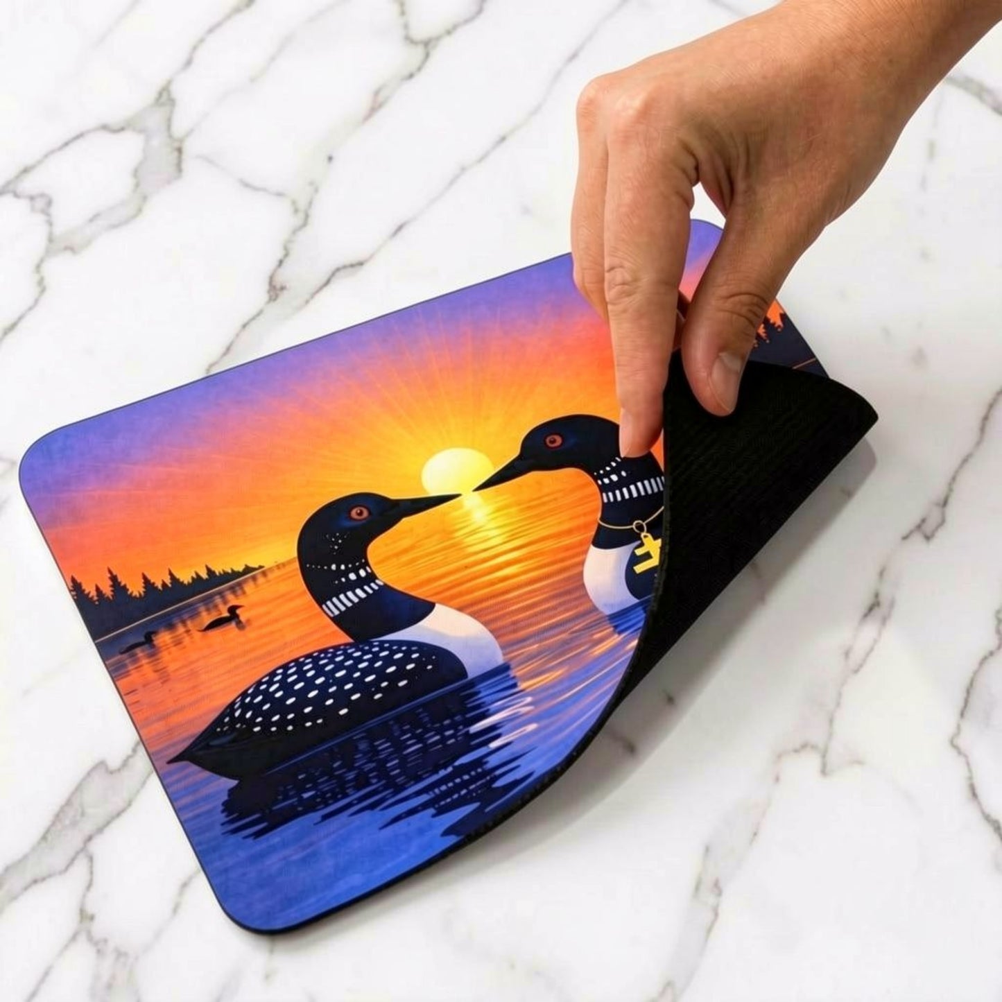 Mouse pad with sunrise loon design on a marble surface, showing the natural rubber base.